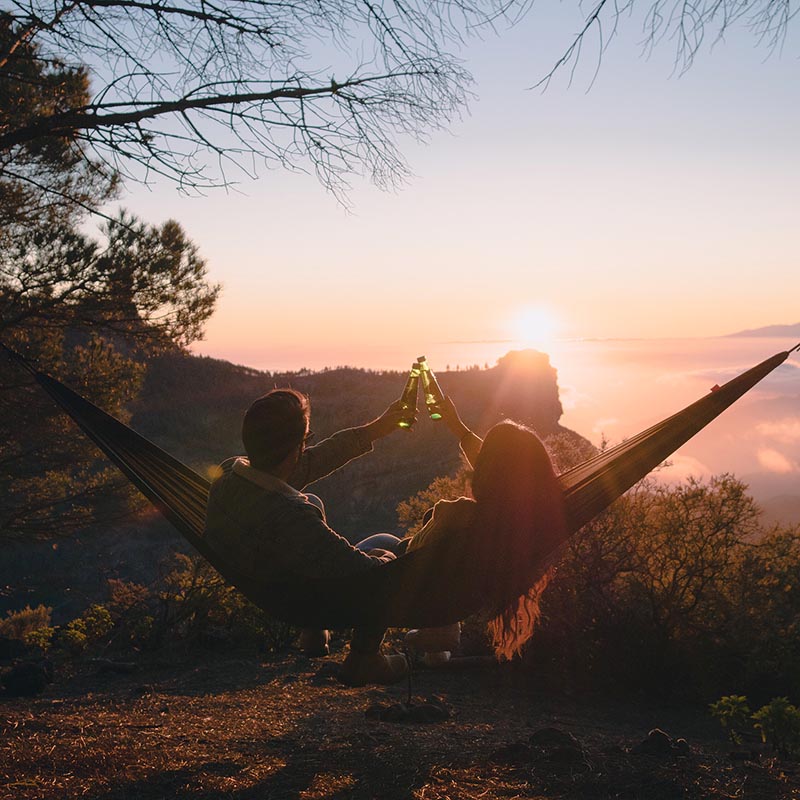 Pareja disfrutando de bebidas en hamaca, en la montaña